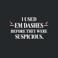 Black serif text on an off-white background reads I USED — EM DASHES — BEFORE THEY WERE SUSPICIOUS, with two red hand-drawn arrows pointing to the em dashes flanking EM DASHES. Artwork shown on the Black garment colour.