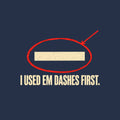 Navy artwork showing a cream em dash circled in red ink with a red leader line pointing to it, above bold cream uppercase text reading I USED EM DASHES FIRST. Artwork shown on the Navy garment colour.