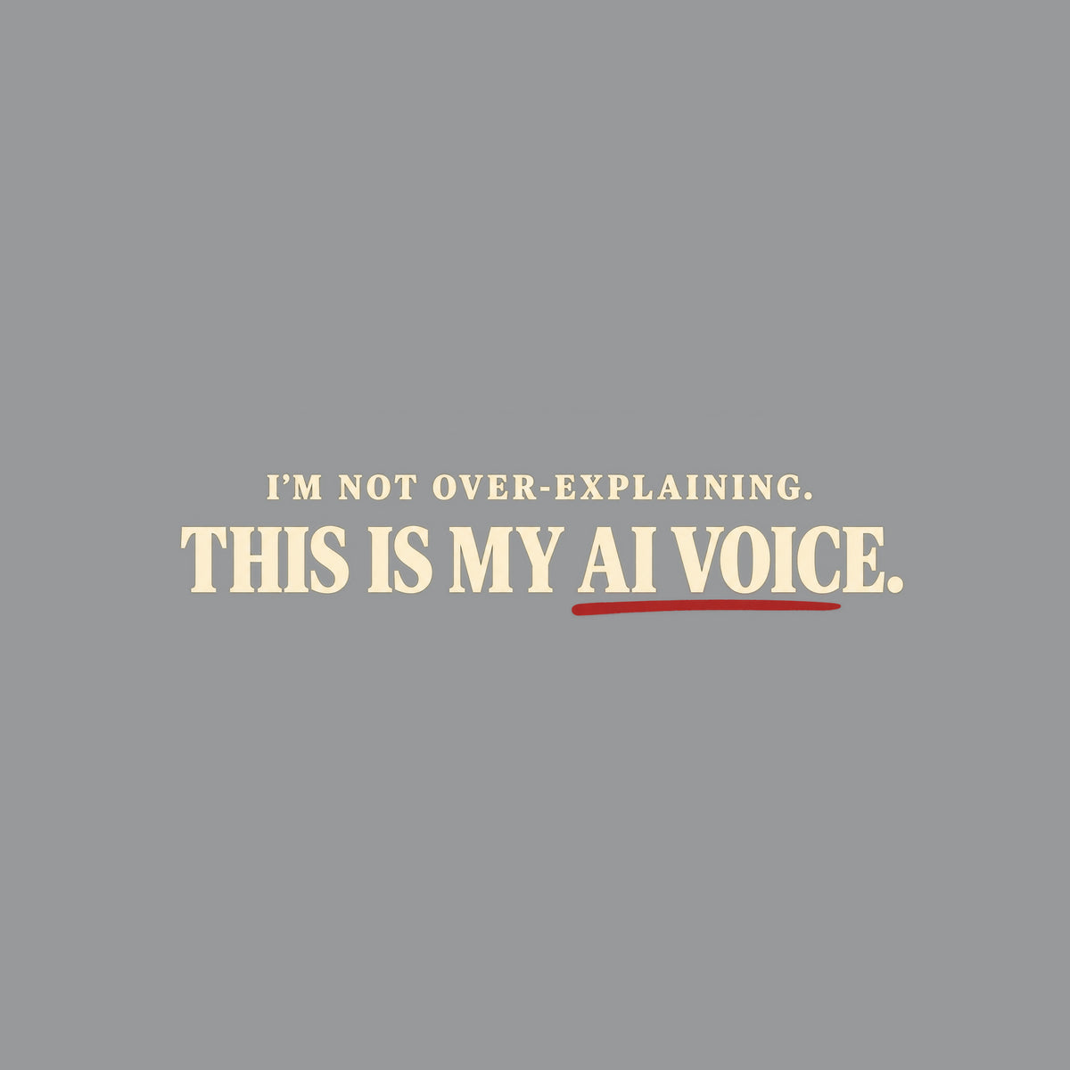 Black tee with cream text reading I'M NOT OVER-EXPLAINING. above larger bold text THIS IS MY AI VOICE. with a muted red underline beneath AI VOICE. Artwork shown on the Sport Grey garment colour.