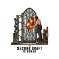 Illustration of a mechanical rig assembling a stained-glass window's pale blue-gray panes while a bearded artisan in an apron installs a glowing ruby, amber and cream center panel by hand. Text below reads THE SECOND DRAFT IS HUMAN. Artwork shown on the White garment colour.