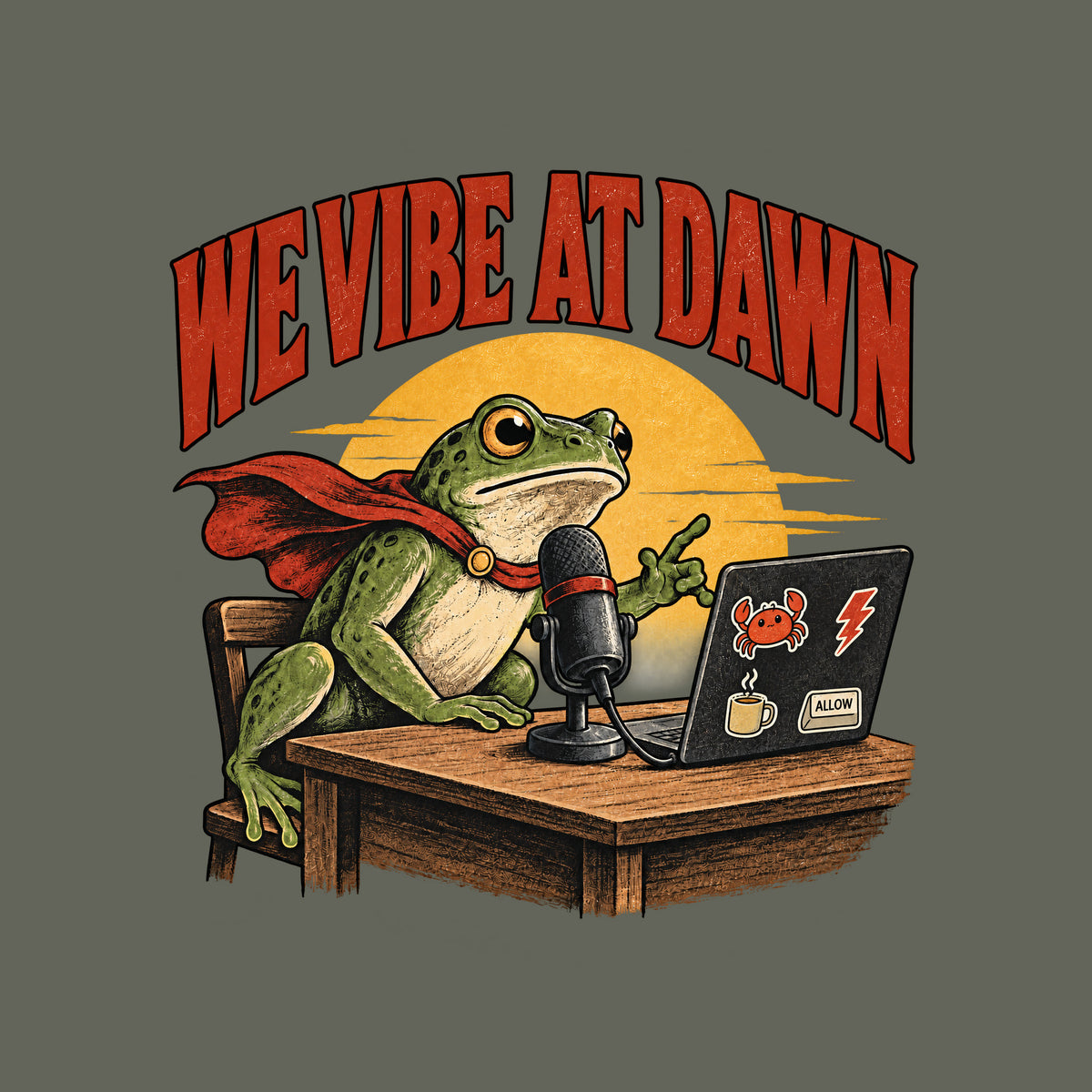 Illustrated frog wearing a red cape sits at a wooden desk before a microphone, one hand raised, beside a laptop with crab, lightning bolt, coffee mug and ALLOW stickers, under a yellow dawn sun and the arched red headline WE VIBE AT DAWN. Artwork shown on the Military Green garment colour.
